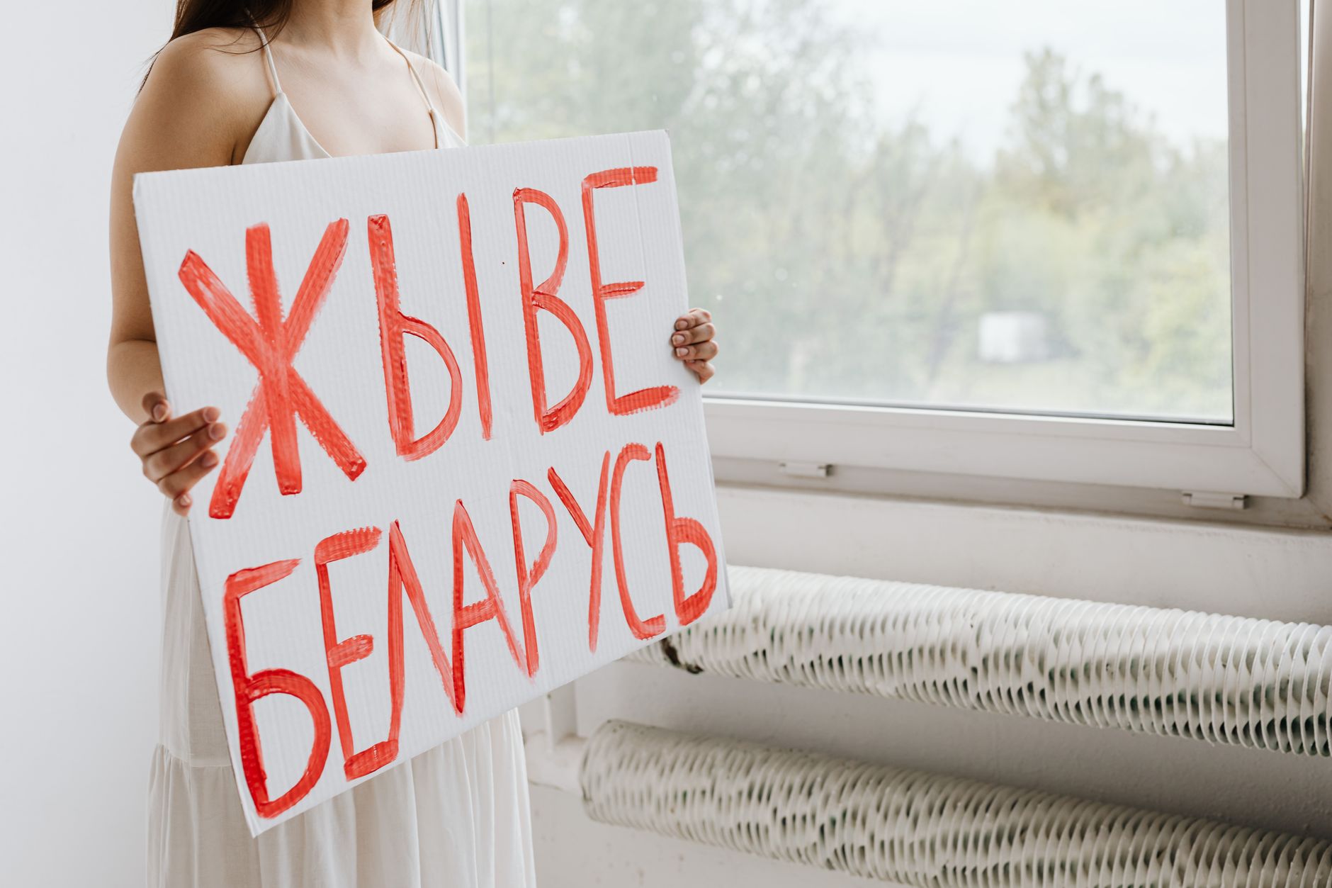 Person holding a handwritten cardboard sign by a window